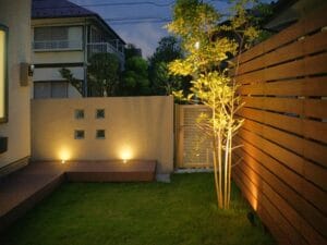 メインガーデンの夜景写真です。  シンボルツリーのシマトネリコをスポットライトでぼんやりと照らし  リビングから楽しめるようにしました。  奥のガラスブロックを埋め込んだ壁の前には  デッキライトで下から壁を柔らかく照らしています。